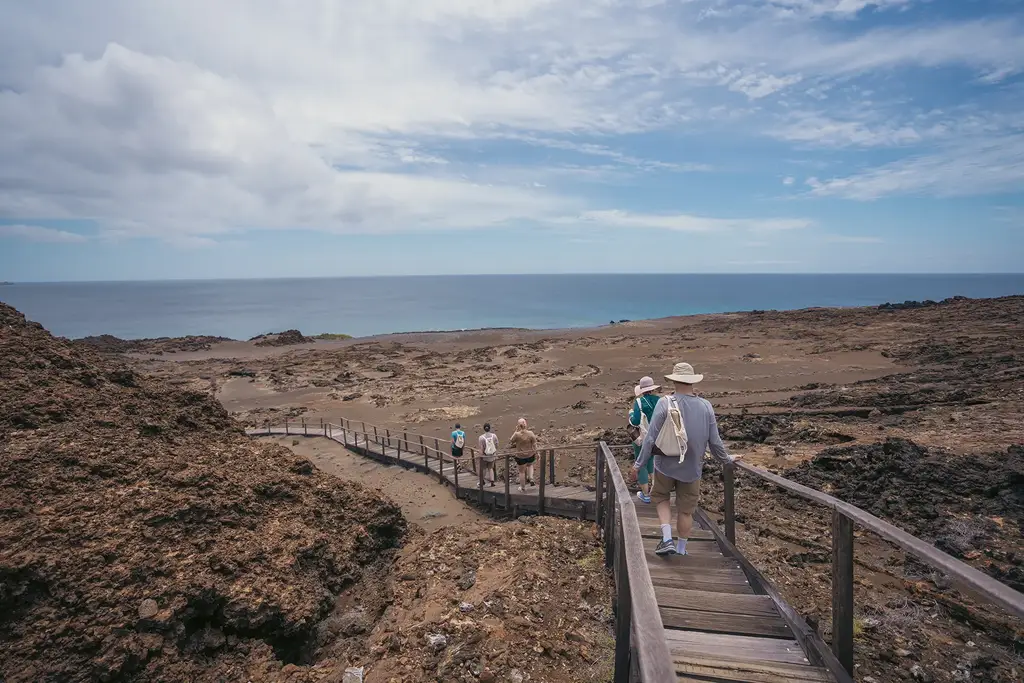 Guests walking a wooden boardwalk across volcanic Galápagos terrain